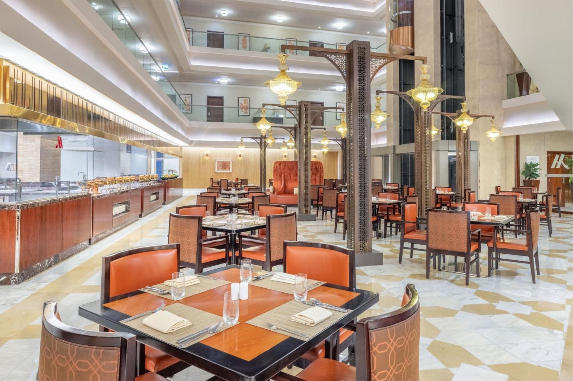 فندق جبل عمر ماريوت مكة المكرمة المظهر الخارجي الصورة The photo depicts an elegant dining area within a restaurant. The space features several tables, each set with plates, glasses, and napkins. The seating consists of brown chairs with orange accents. The restaurant has a modern design, highlighted by 